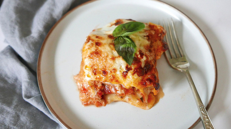 Portion of lasagna on plate, topped with basil leaves