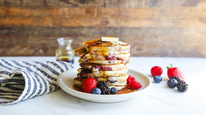 Stack of berry buttermilk pancakes on plate with fresh berries, butter, and syrup