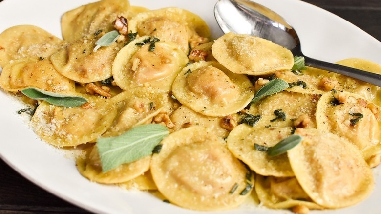 Butternut squash ravioli on white plate with spoon and fresh sage leaves.