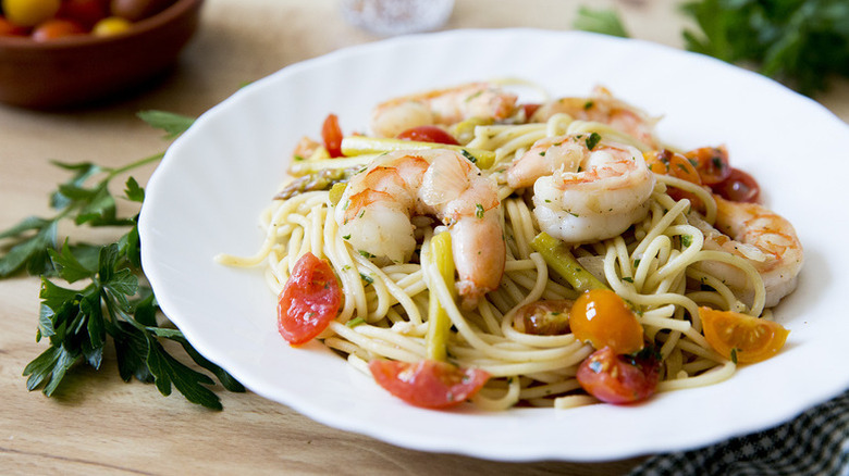Spaghetti with shrimp, tomatoes, and asparagus in white dish.