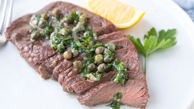Sliced flat iron steak on plate, topped with herbs and capers.