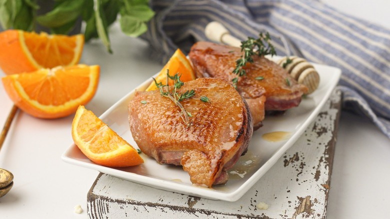 Honey-glazed duck breasts on plate with orange wedges and thyme sprigs.
