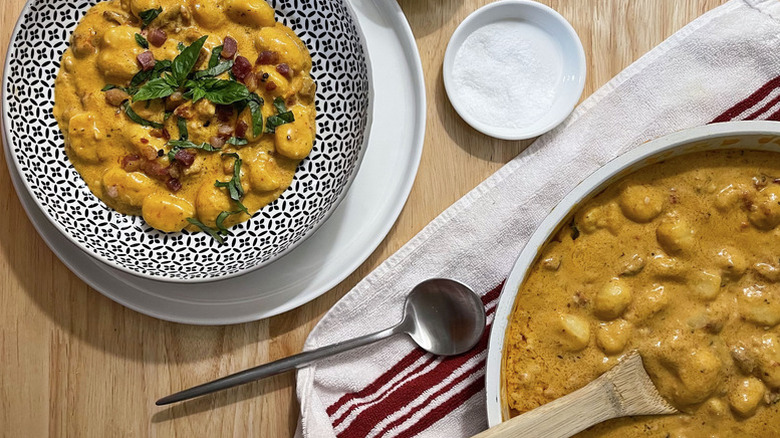 Creamy gnocchi served into bowl, topped with pancetta and fresh basil.