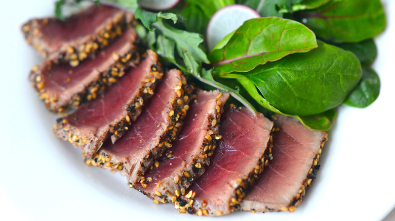 Peppercorn-crusted sliced tuna steak on plate with salad.