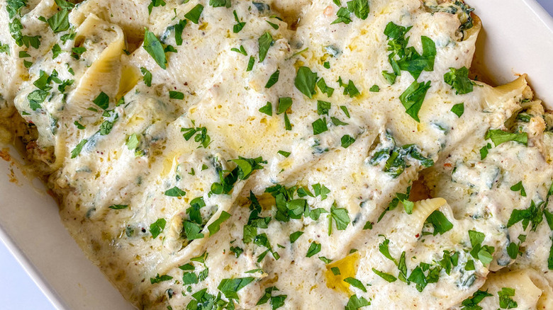 Creamy stuffed shells in baking dish, topped with fresh parsley.