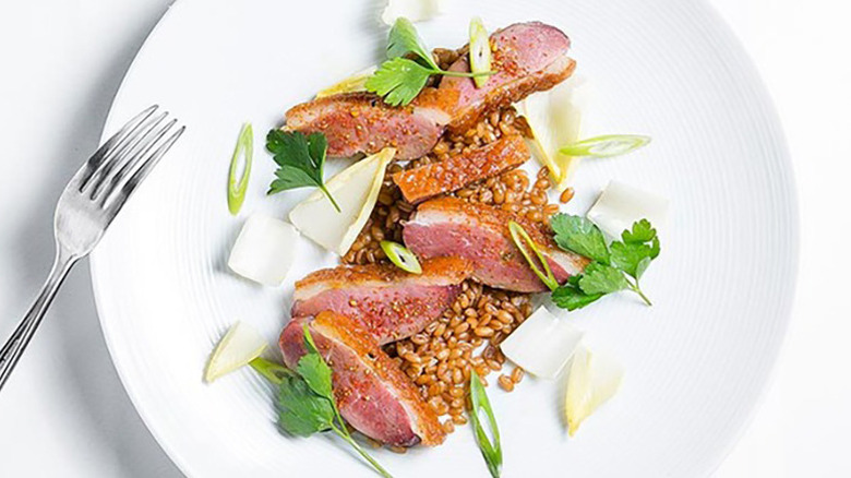 Sliced seared duck breast on plate with endive and wheat berries.