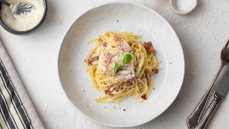 Spaghetti carbonara in bowl, topped with fresh basil.