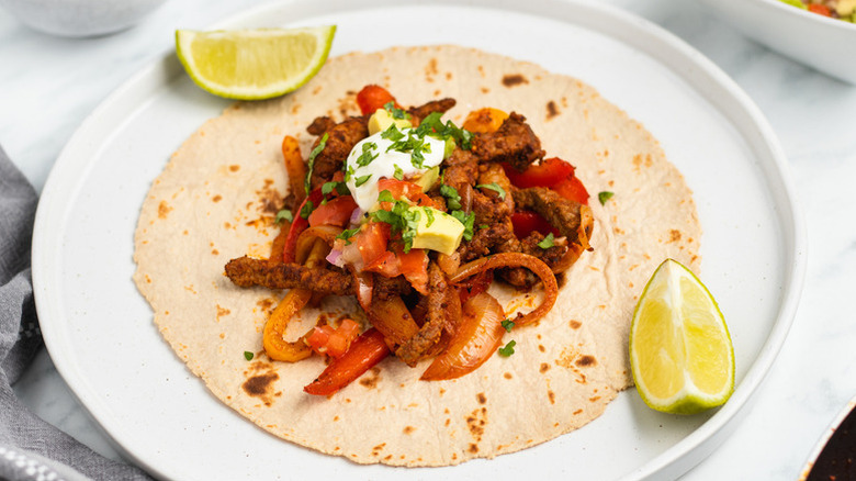 Steak, pepper, and onion fajita on plate, topped with avocado, sour cream, and cilantro.