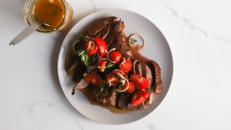 Sliced flank steak on plate, topped with tomato vinaigrette and fresh tomatoes.