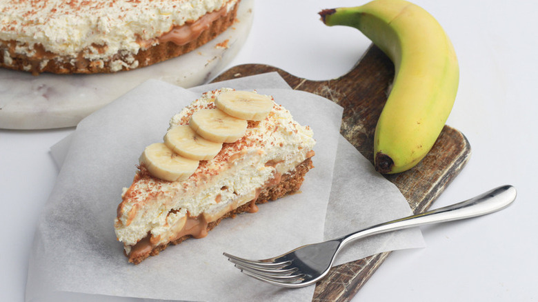 Slice of banoffee pie on a parchment-lined wooden cutting board