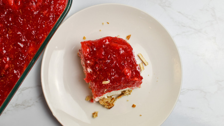 Slice of strawberry pretzel salad on a plate next to a glass dish