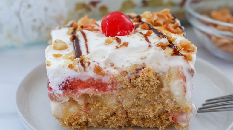 Slice of banana split cake on a plate, topped with a maraschino cherry