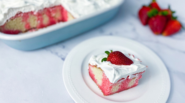Slice of Jell-O poke cake on a plate, topped with a fresh strawberry half
