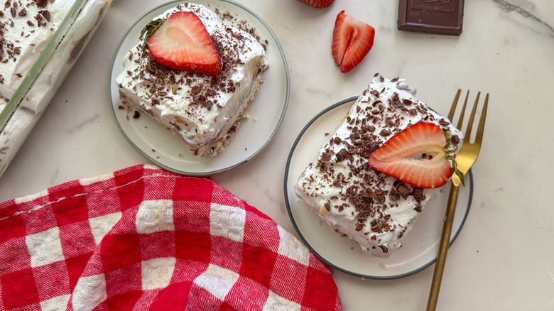 Two slices of creamy Robert Redford cake on plates, topped with fresh strawberries and chocolate shavings