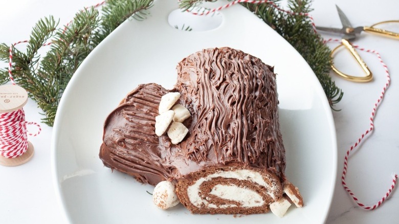 Chocolate yule log on a plate next to pine tree sprigs
