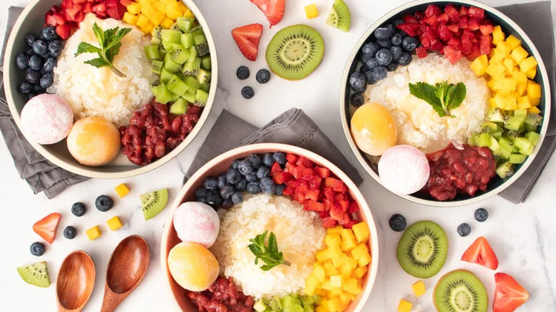 Patbingsu (Korean Shaved Ice) in three bowls surrounded by cut fruit