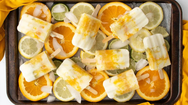 Triple Citrus Yogurt Popsicles on baking sheet with citrus slices