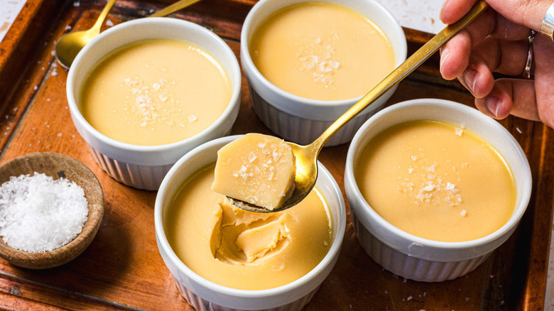 Spooning salted caramel panna cotta from ramekin with three more ramekins on the side