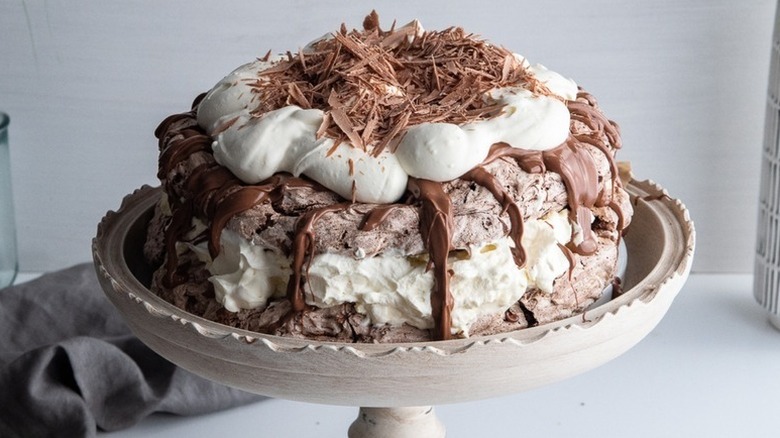 Chocolate pavlova on cake stand, topped with whipped cream and chocolate shavings