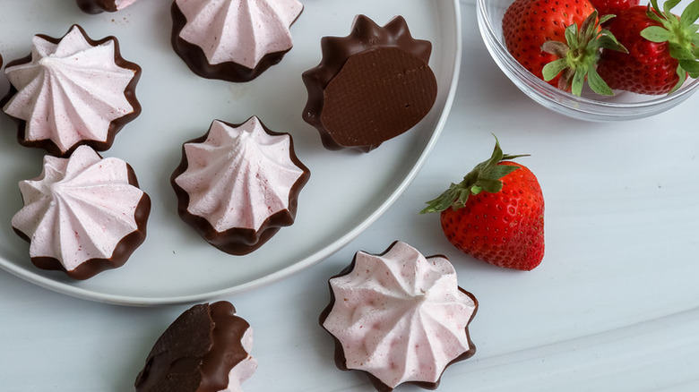 Chocolate-dipped strawberry meringue cookies on plate next to bowl of strawberries