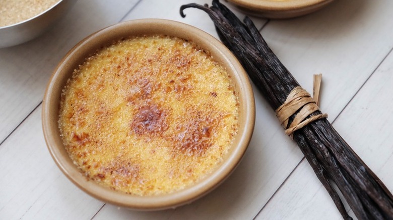 Creme brulee in ramekin next to bundle of vanilla pods