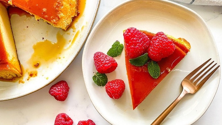 Cuban flan served onto plate and topped with fresh raspberries with the rest of the flan on the side