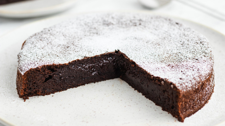 Showing a center of flourless chocolate torte that's served on a a plate, dusted with powdered sugar