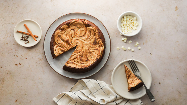 Top view of gingerbread white chocolate cake sliced and served onto plate with spices and white chocolate chips in bowls on the side
