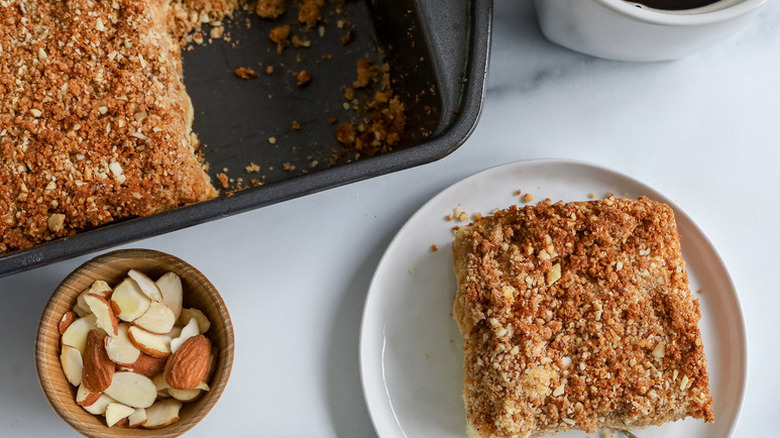 Almond coffee cake served from baking pan onto plate with some slivered almonds in a bowl next to it