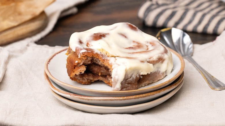 Frosting-topped cinnamon roll with a bite taken out served on plate with a spoon