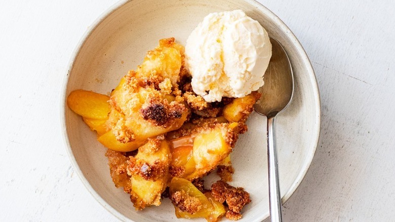 Top view of peach crisp in bowl served with scoop of vanilla ice cream