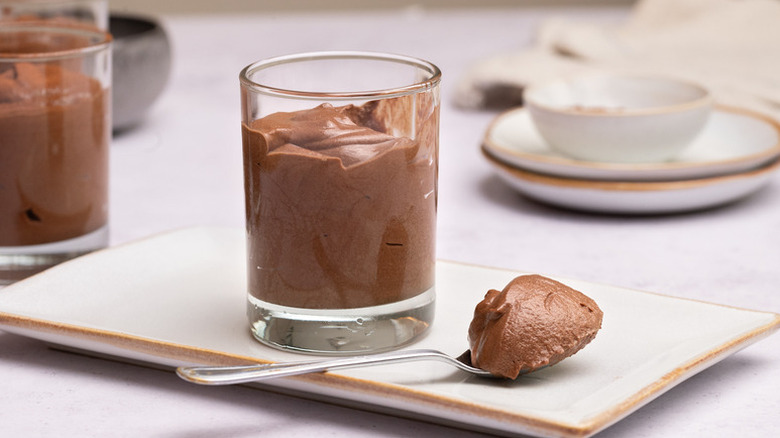 Chocolate mousse in glass with spoonful on the side and more glasses in the back