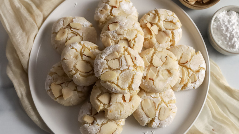 Top view of a plate of almond crinkle cookies on plate with powdered sugar on the side