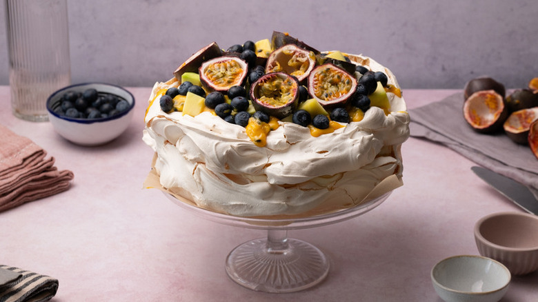 Pavlova on cake stand, topped with passion fruit, blueberries, and mango