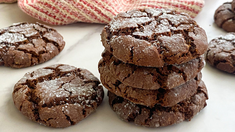 Stack of chocolate crinkle cookies coated in sugar with cookies placed around the stack