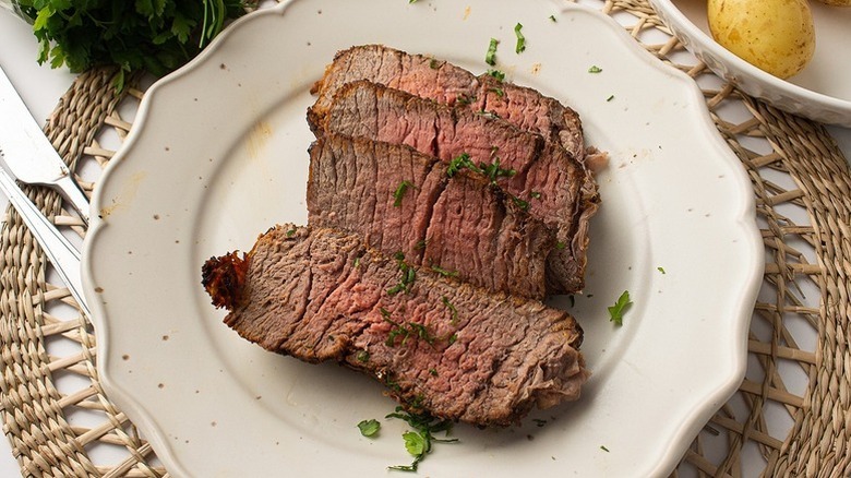 Sliced roast beef on plate with fresh herb garnish
