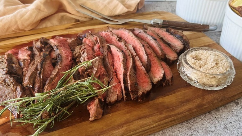 Grilled sliced flank steak on wooden serving board with fresh rosemary