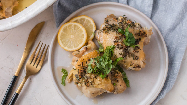 Herby baked chicken thighs on plate with lemon rounds