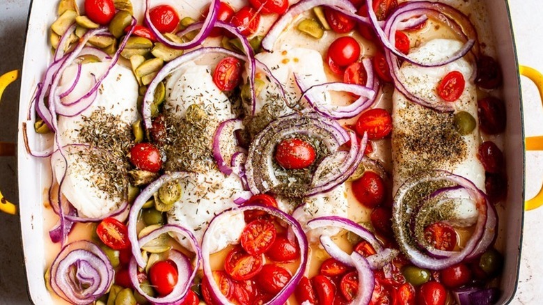 Herby baked cod fillets in baking dish with roasted cherry tomatoes, olives, and red onion