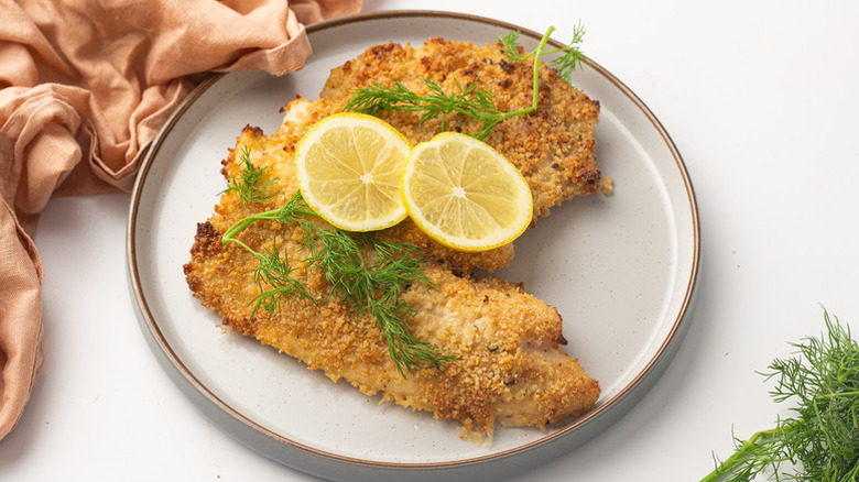 Parmesan crusted tilapia on plate with dill sprigs and lemon rounds