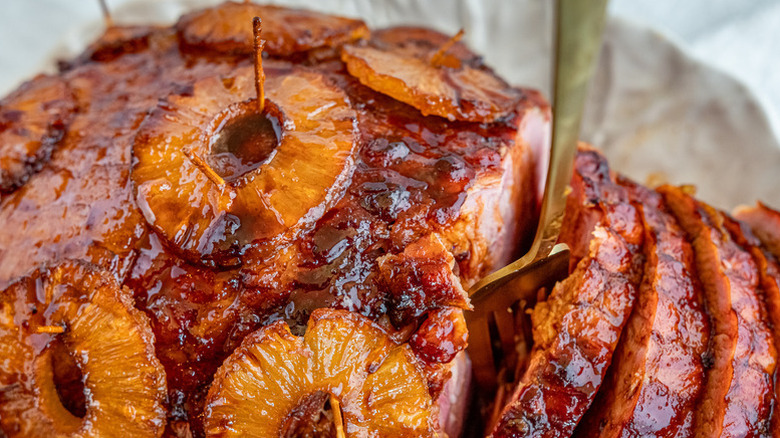 Fork digging into sliced glazed ham with pineapple rings
