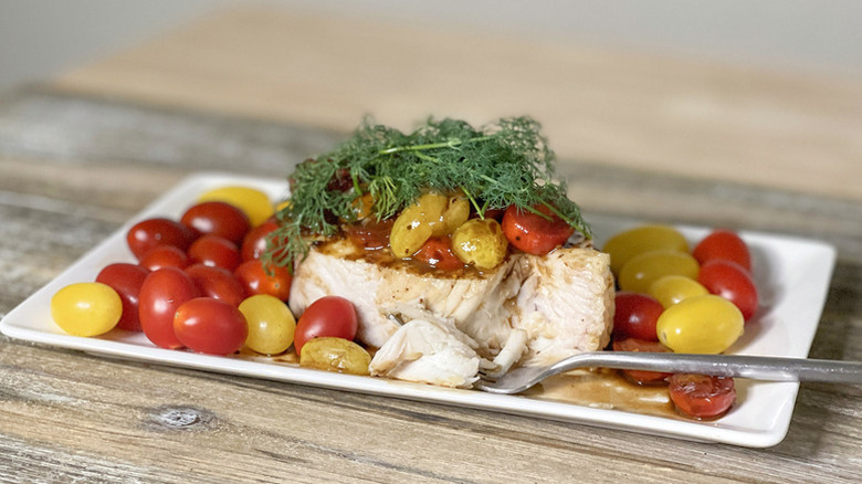 Baked halibut on plate with balsamic cherry tomatoes and dill