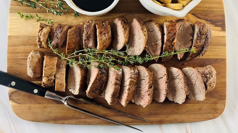 Sliced pork tenderloin on wooden board with sprigs of thyme