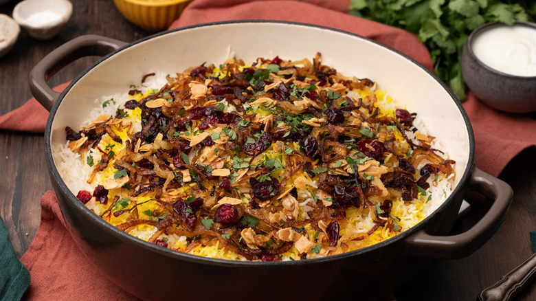 Lamb biryani in casserole pan, topped with fried almonds and dried cranberries