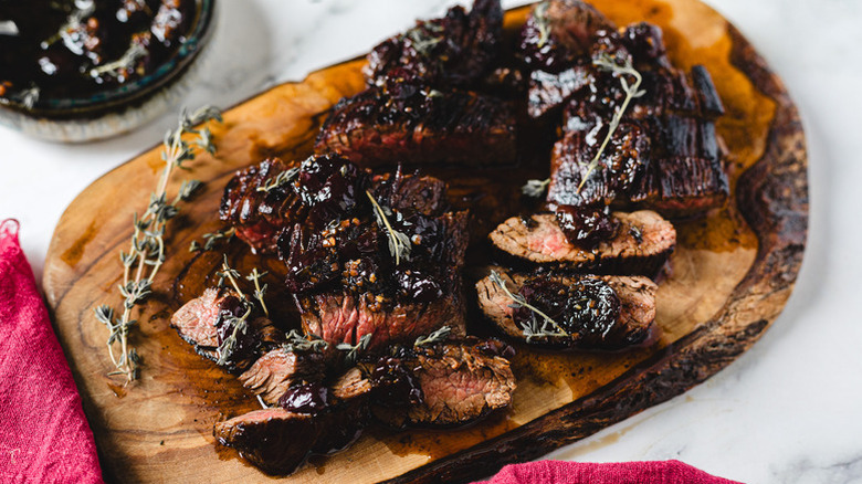 Sliced steak on wooden board, topped with cherry balsamic sauce
