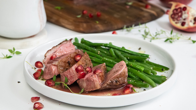 Sliced duck breast on plate with pomegranate sauce and green beans