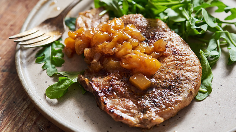 Seared pork chop on plate with peach chutney and fresh arugula