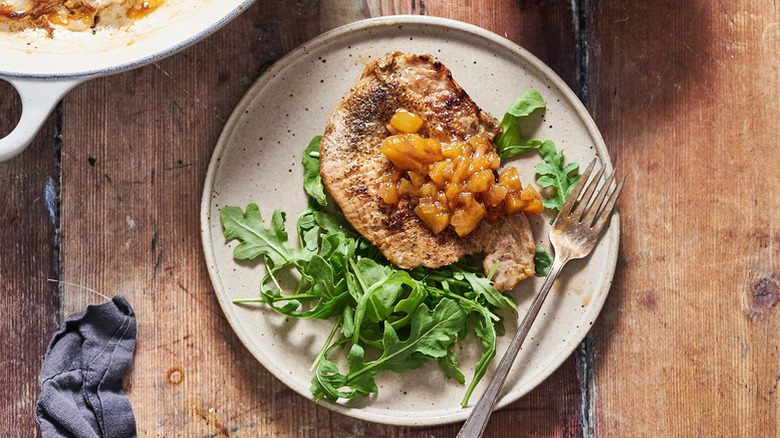 Pork chop on plate with peach chutney and fresh arugula