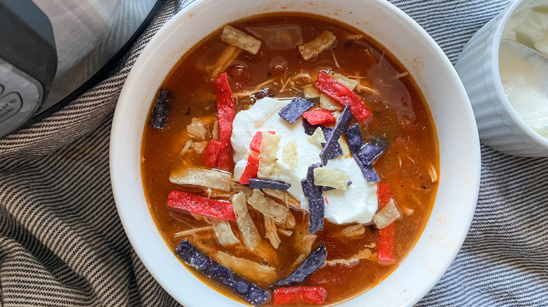 Bowl of Instant Pot tortilla soup topped with sour cream and tortilla strips