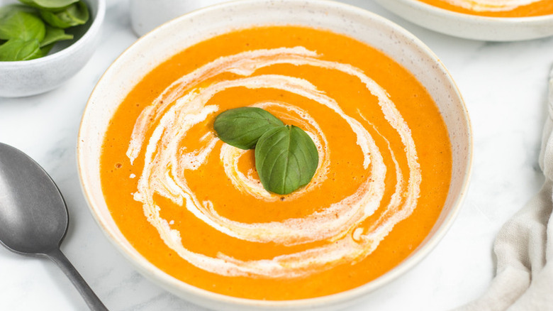 Bowl of roasted tomato soup garnished with cream and basil